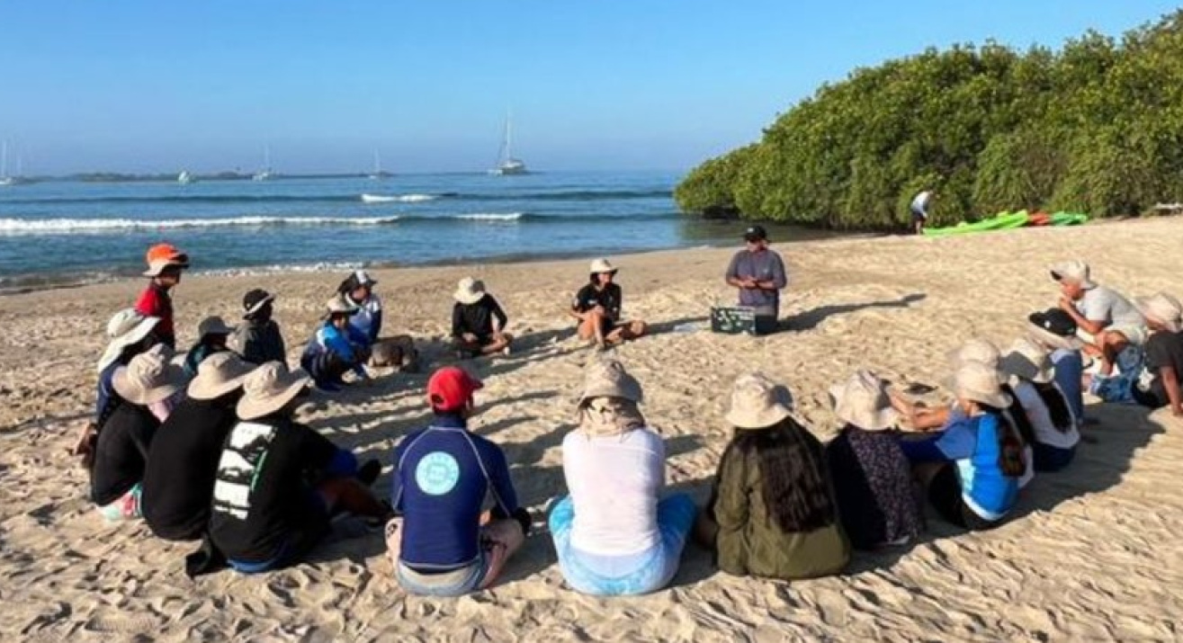 Niños participantes del proyecto Naveducando, sentados en formación circular en la arena de la playa